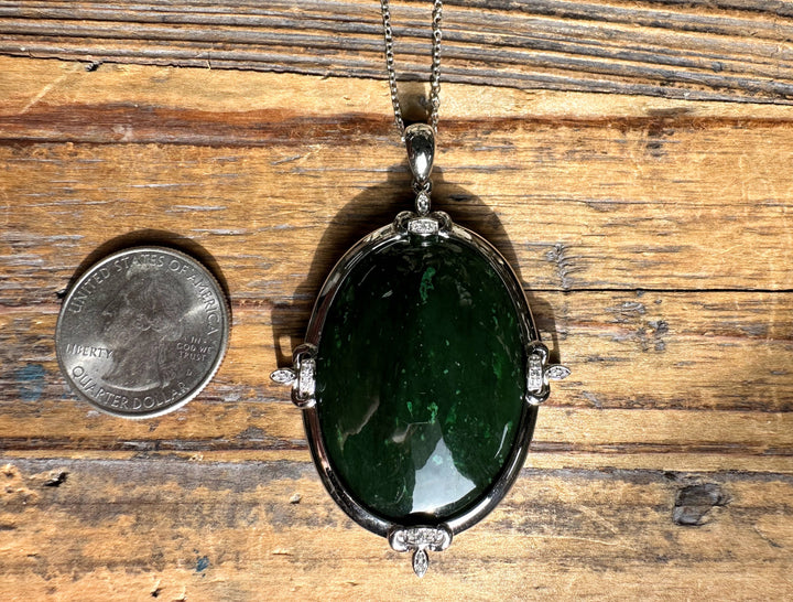 Oval jade pendant with silver frame and zircon accents shown beside a US quarter for scale on wood