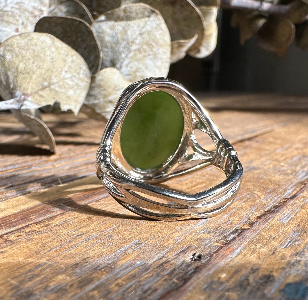 Green jade oval set in a silver ring with a decorative wrap on a rustic wooden surface.