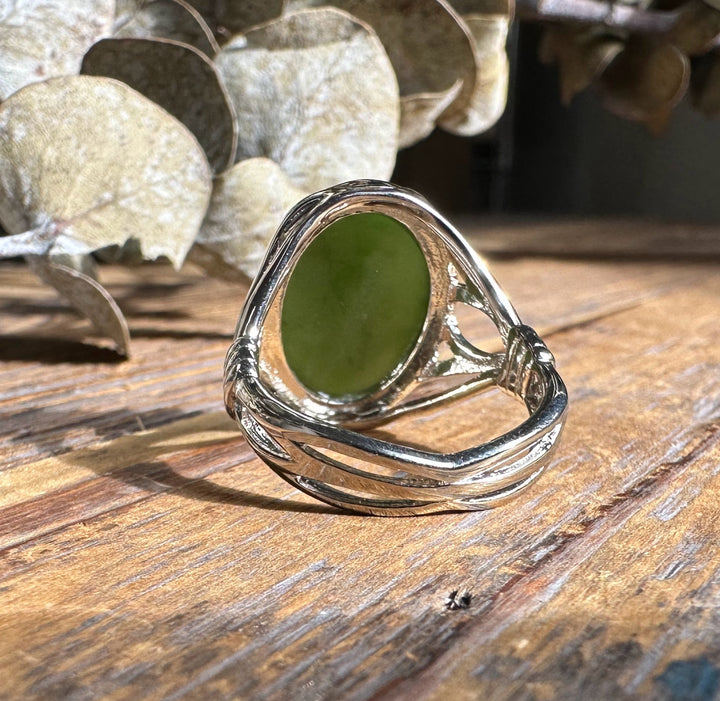 Green jade oval set in a silver ring with a decorative wrap on a rustic wooden surface.