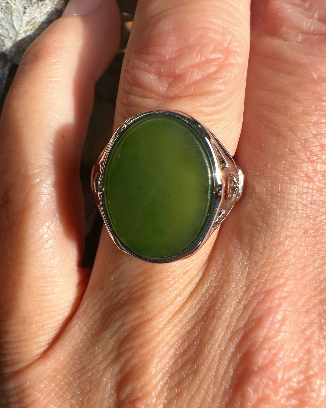 Close-up of the ring worn on a finger showing the green jade centerpiece and ornate silver setting