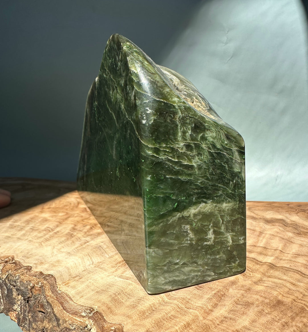 Green jade candle holder shaped as a tall block with a pointed peak on top and a glossy surface on a wood base