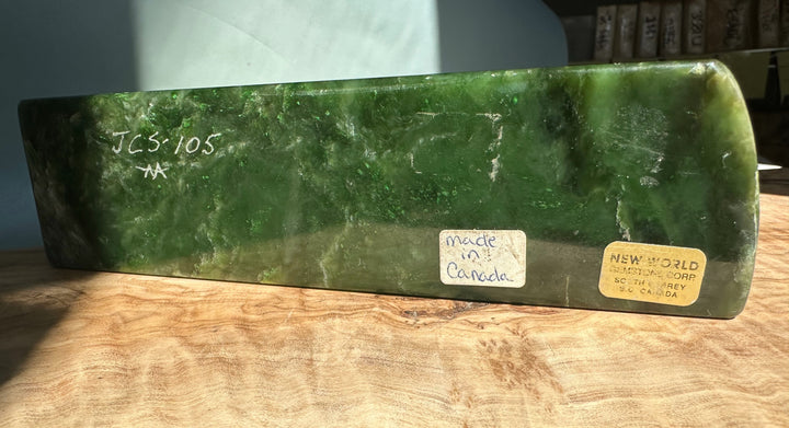 Green jade candle holder specimen in a rectangular block with labels on its surface on a wooden table.