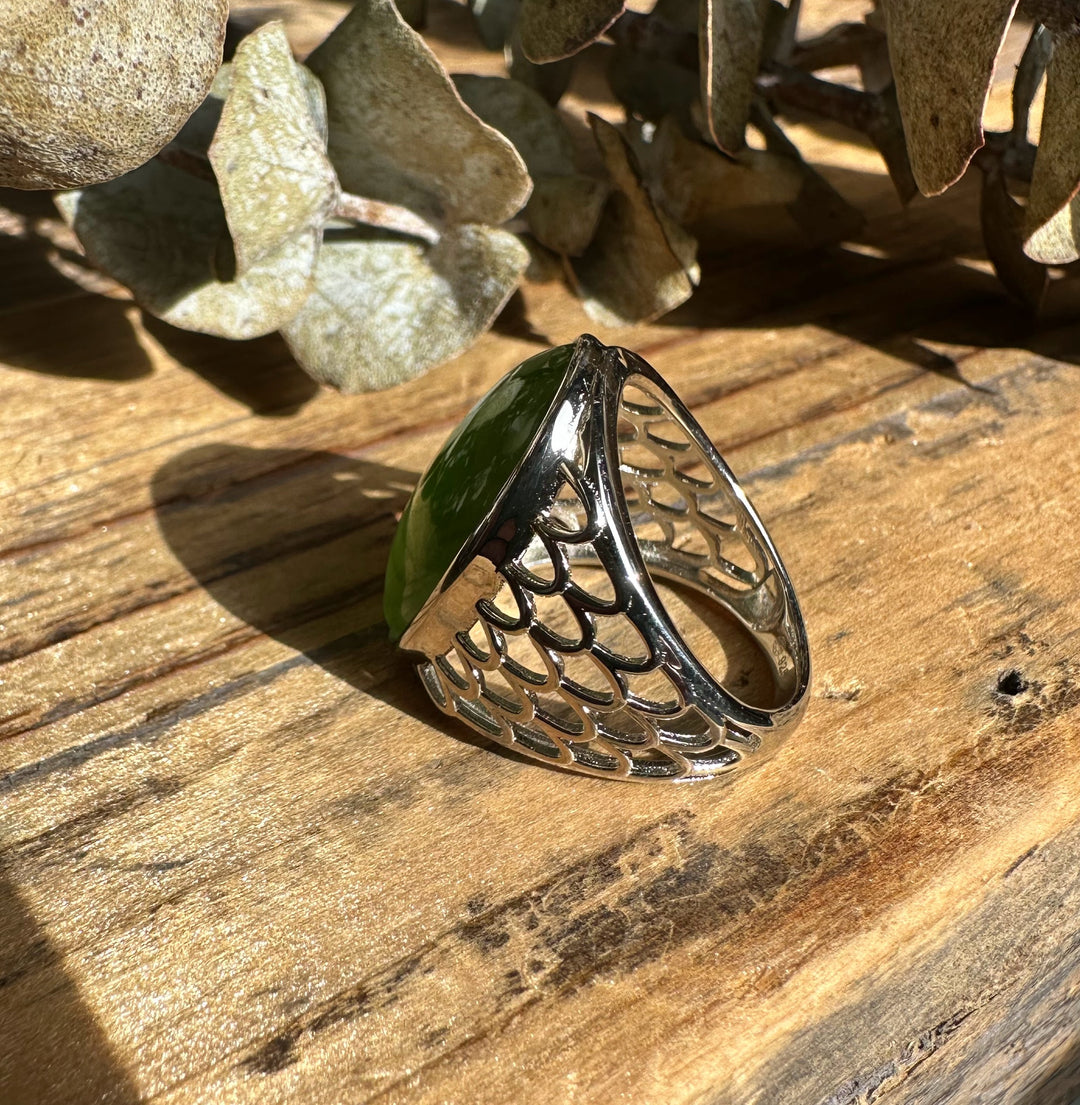 Canadian Jade Ring 2570 featuring an oval green jade cabochon set in a decorative silver lattice band on a wooden surface.