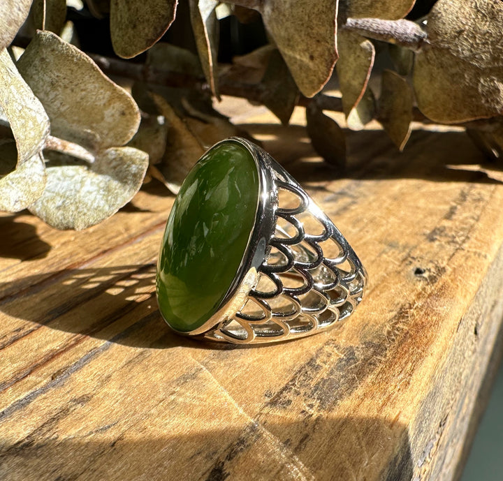 Closeup of Canadian Jade Ring 2570 showing the oval green jade and intricate silver lattice band on a wooden surface.
