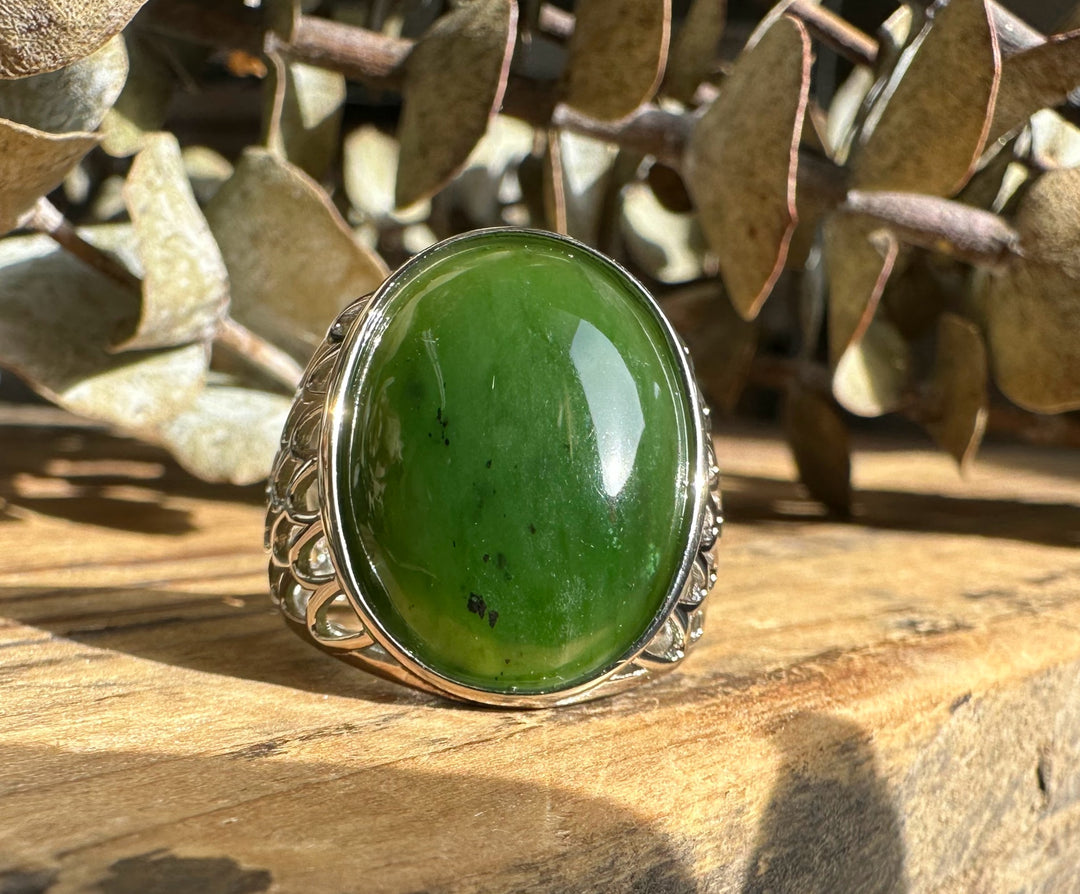 Oval green Canadian jade ring with a silver bezel and decorative split shank on a wood surface.
