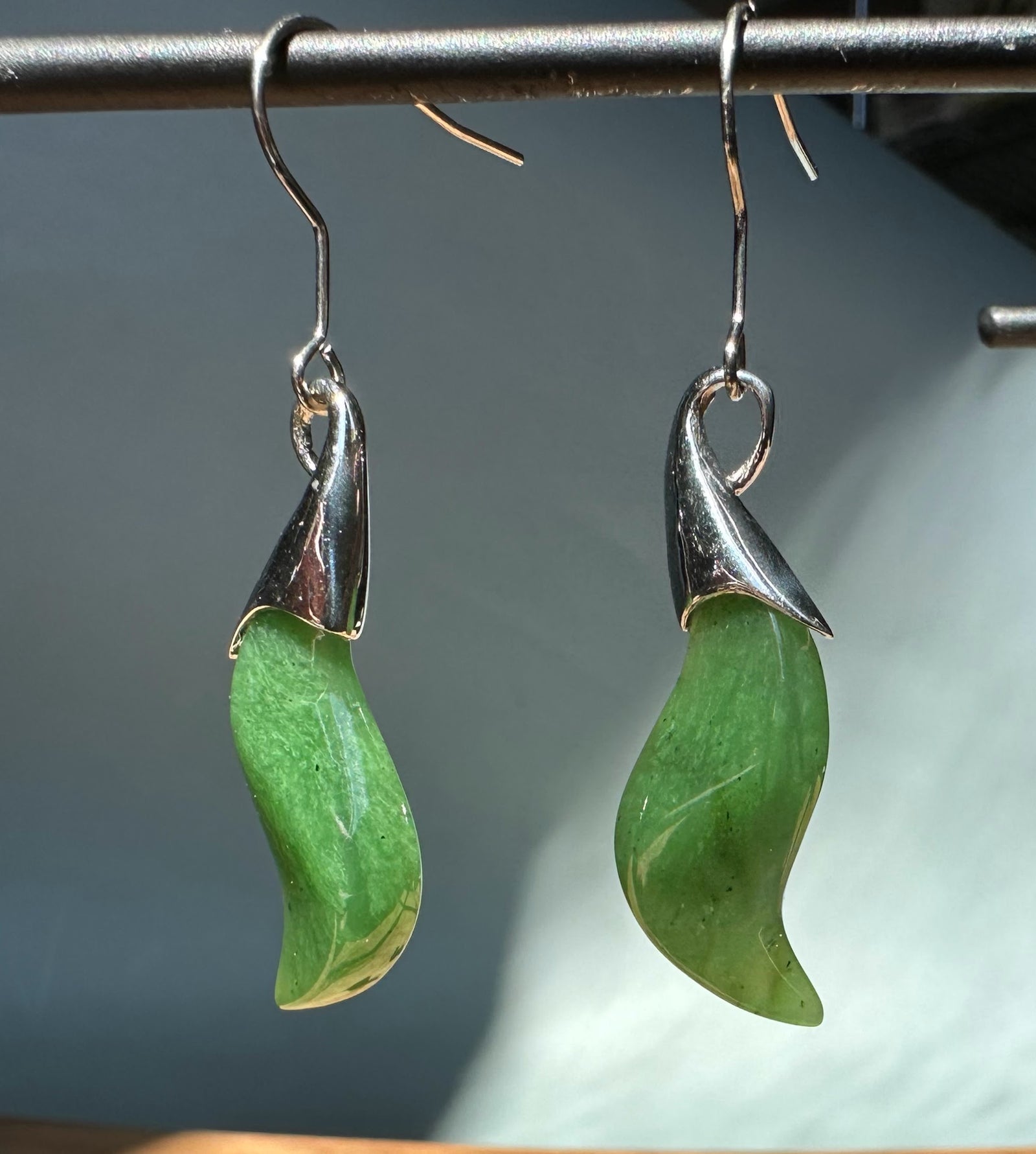 Nephrite jade earrings with curved green drops topped by silver leaf caps and slender hooks