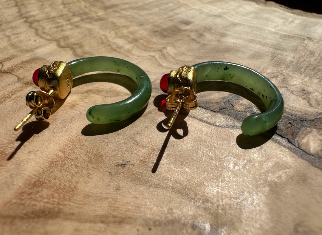 Jade hoop earrings with gold caps and red cabochons, posts visible on a wood surface.