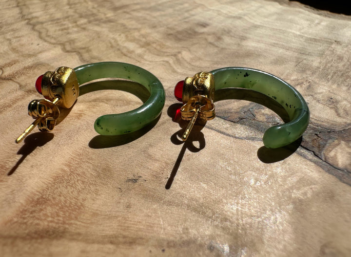 Jade hoop earrings with gold caps and red cabochons, posts visible on a wood surface.