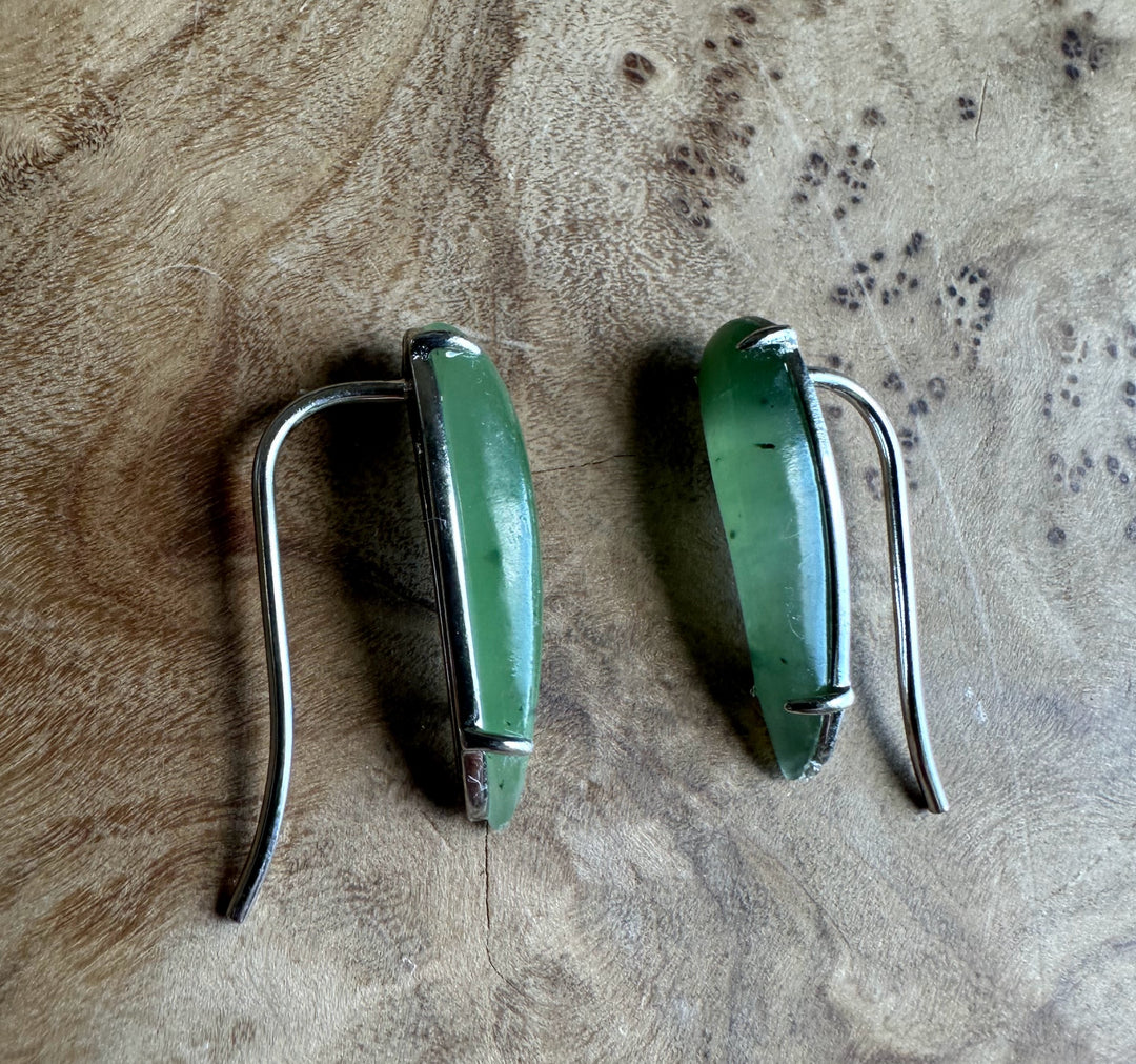 Pair of green earrings with silver hooks on a textured brown surface