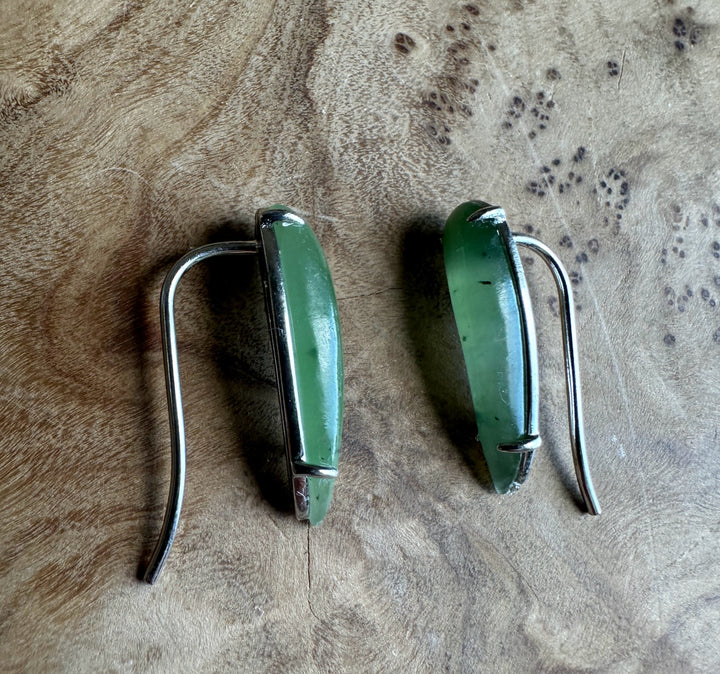 Pair of green earrings with silver hooks on a textured brown surface