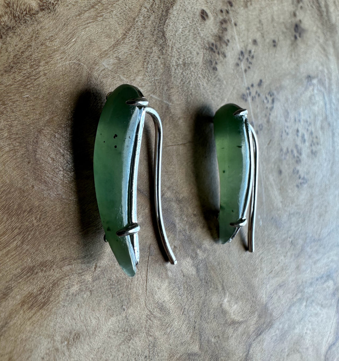 Pair of green and silver earrings on a textured surface