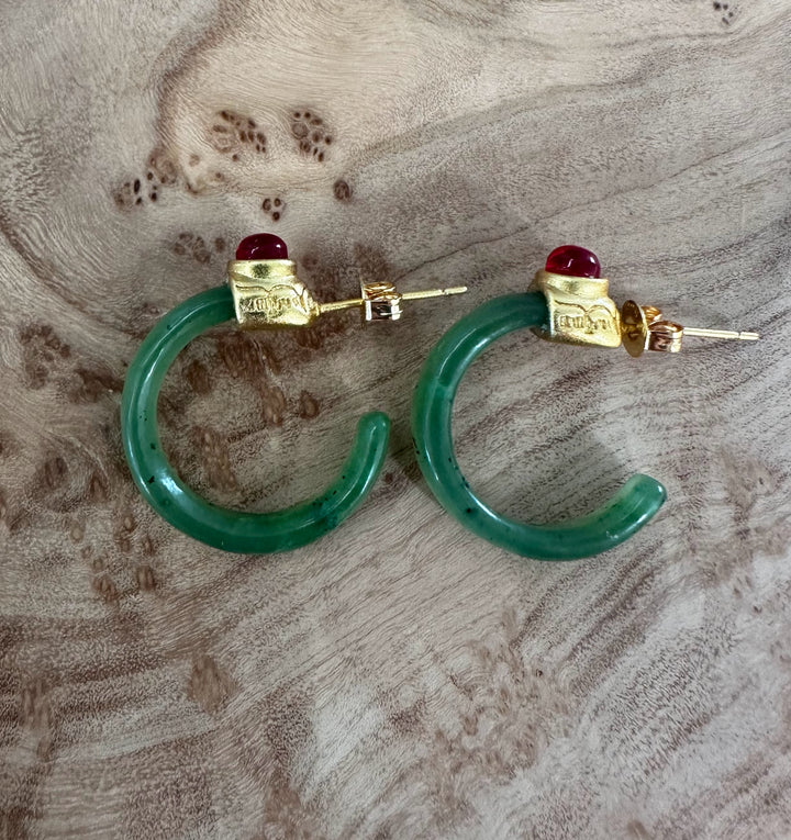 Pair of jade hoop earrings with gold tops and red cabochons on a wood grain backdrop.