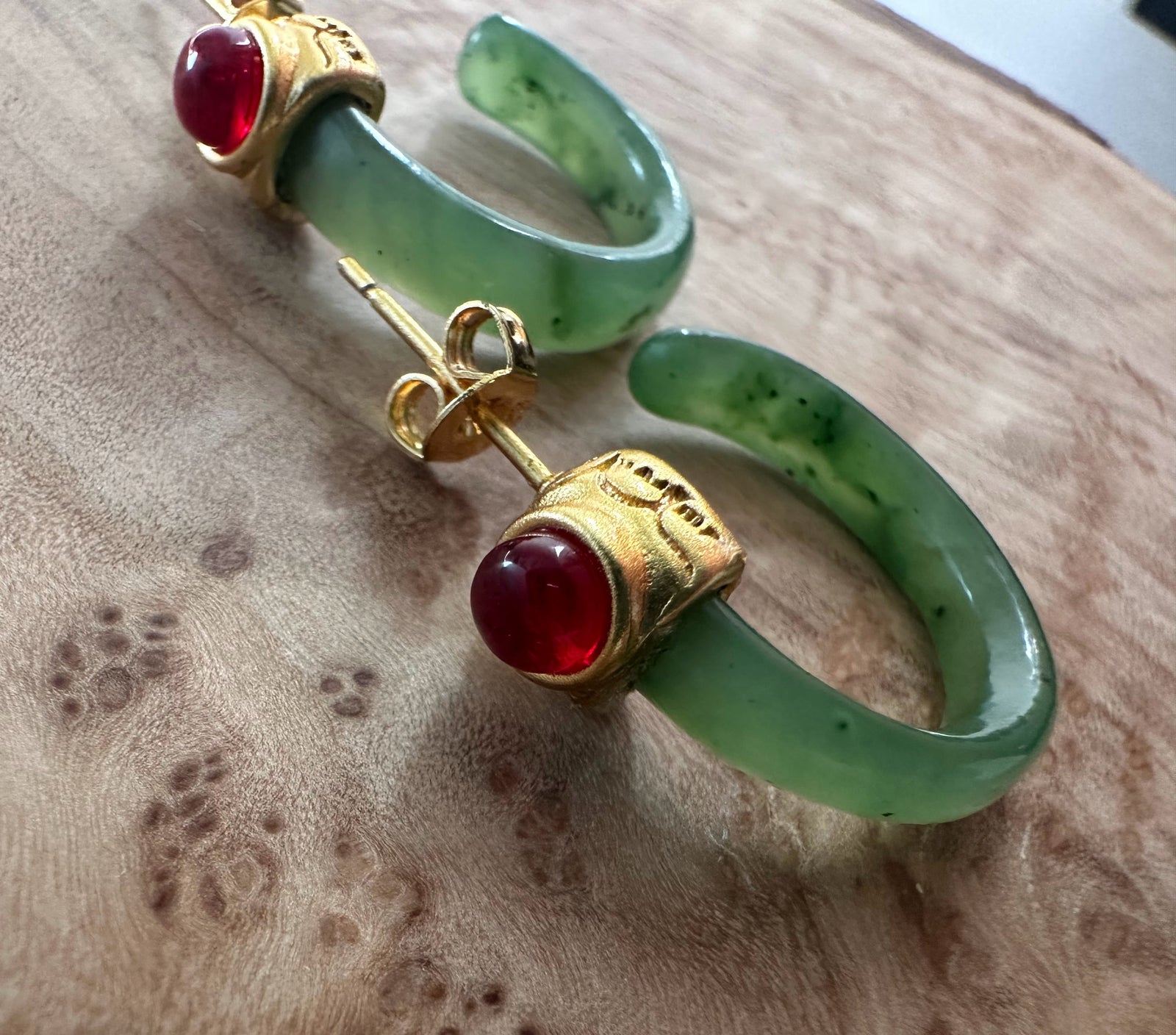 Green jade bracelet with a gold ring set with a red cabochon on a suede surface
