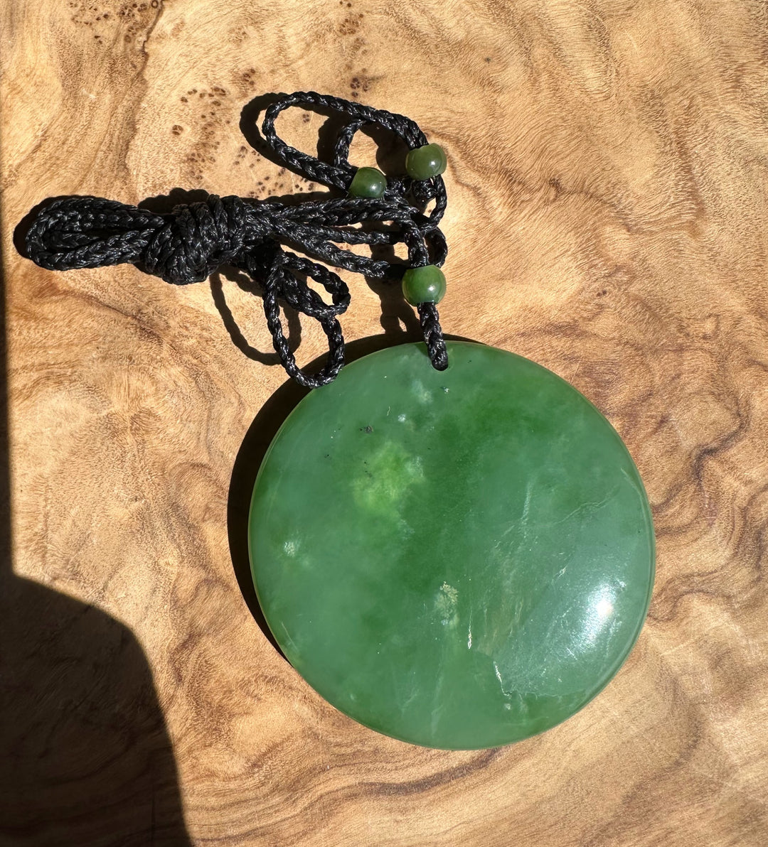 Green jade pendant on a black cord against a wooden background