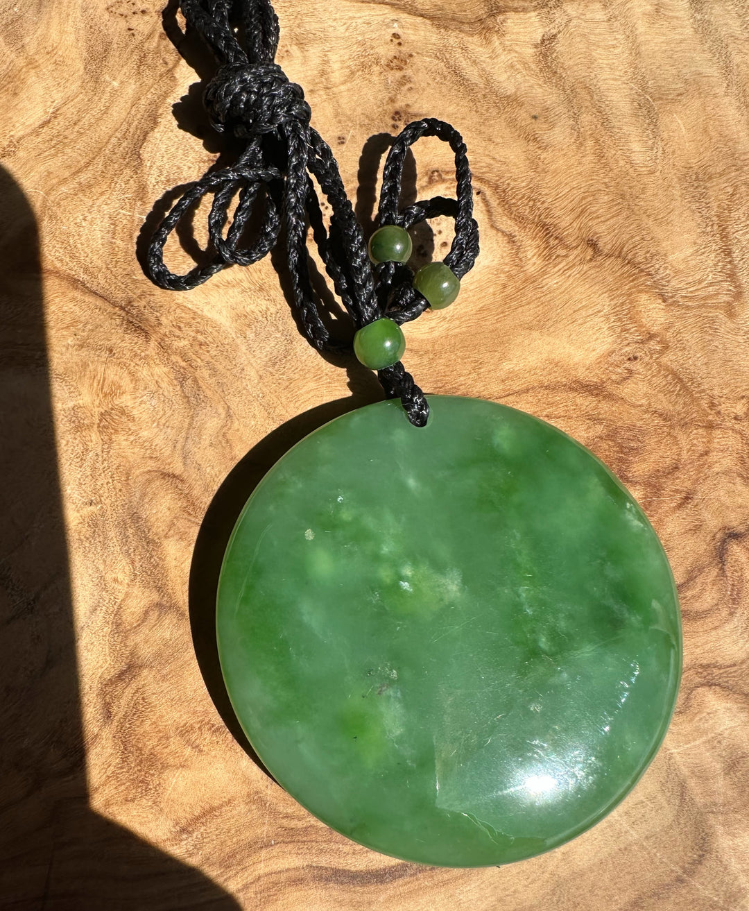 Green jade pendant on a black cord against a wooden background