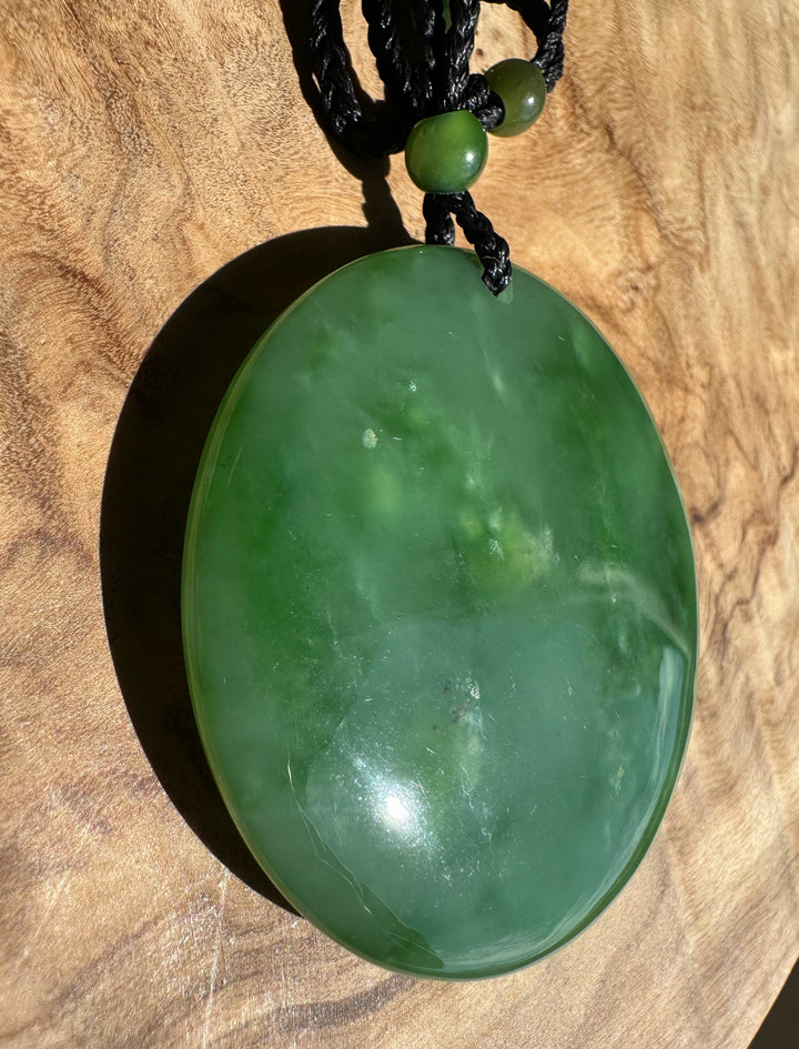 Green jade pendant on a black cord against a wooden background