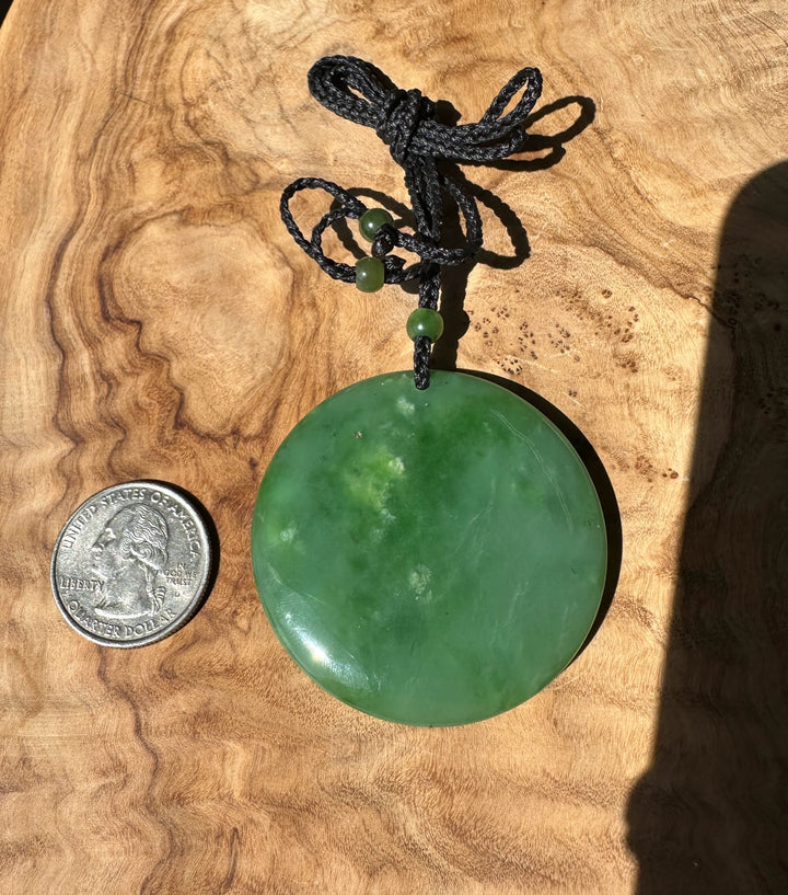 Green jade pendant on a wooden surface with a coin for scale