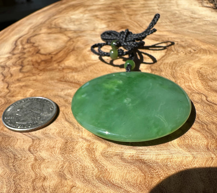 Green jade pendant on a wooden surface with a coin for scale
