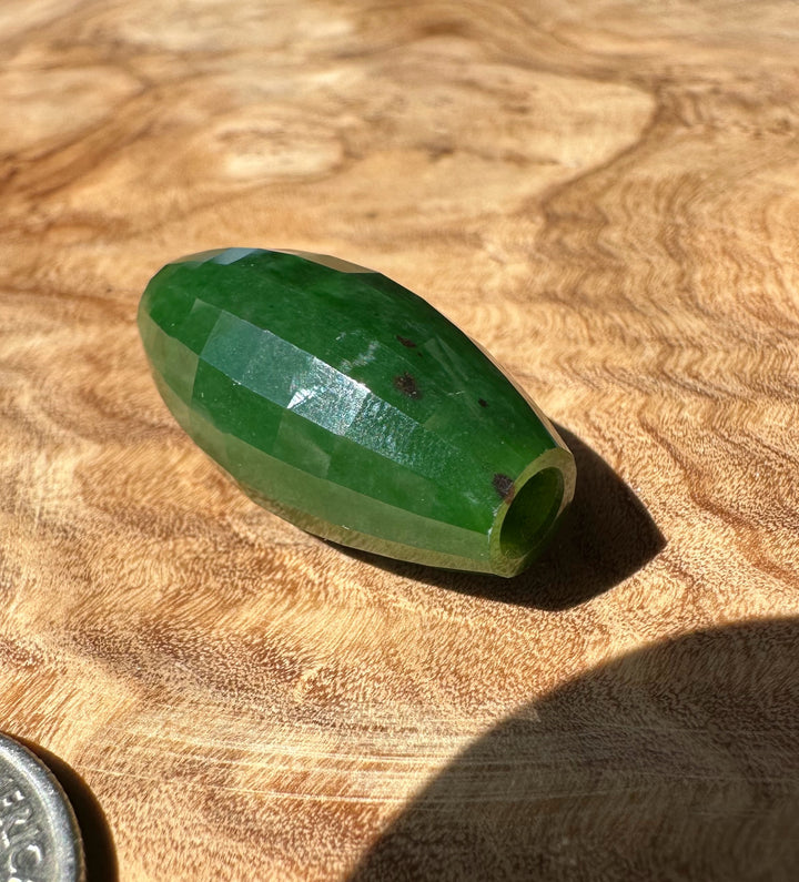 Green jade bead on a wooden surface with a coin for scale