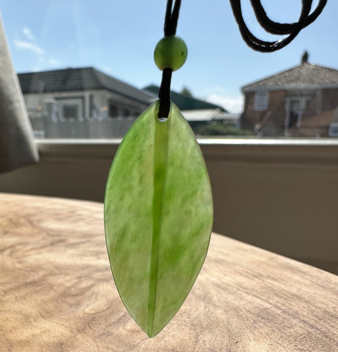 Siberian Jade Leaf Pendant on black cord with green bead hanging outdoors against a blue sky background
