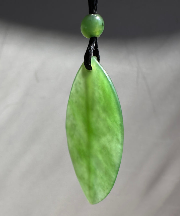 Siberian Jade Leaf Pendant close up with a green bead on braided black cord against a blurred background