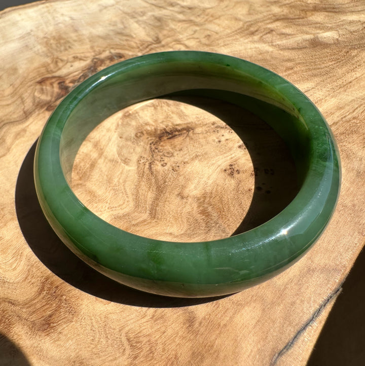 Top close up of a green jade bangle on wood, focusing on the inner curve and glossy finish