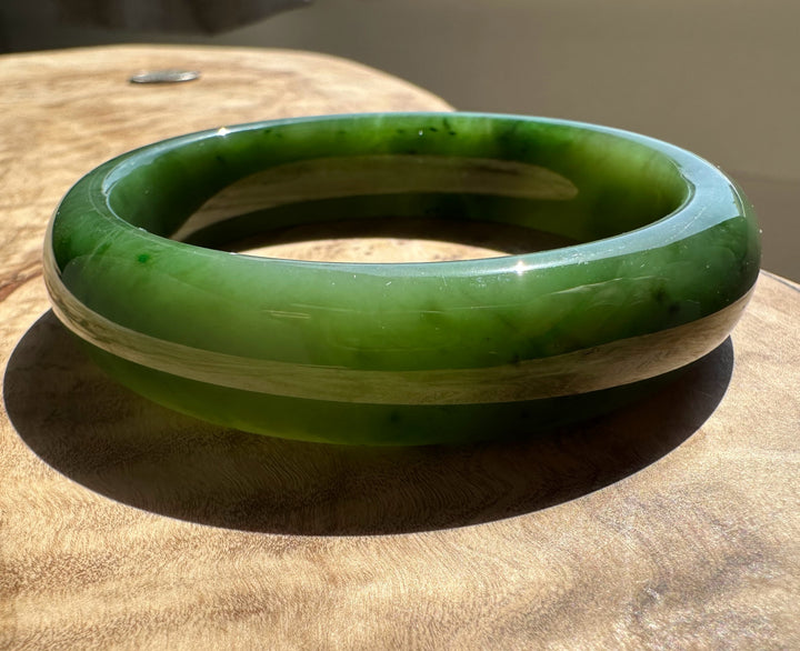 Close up of a green jade bangle resting on a wooden surface, showing its smooth polished edge