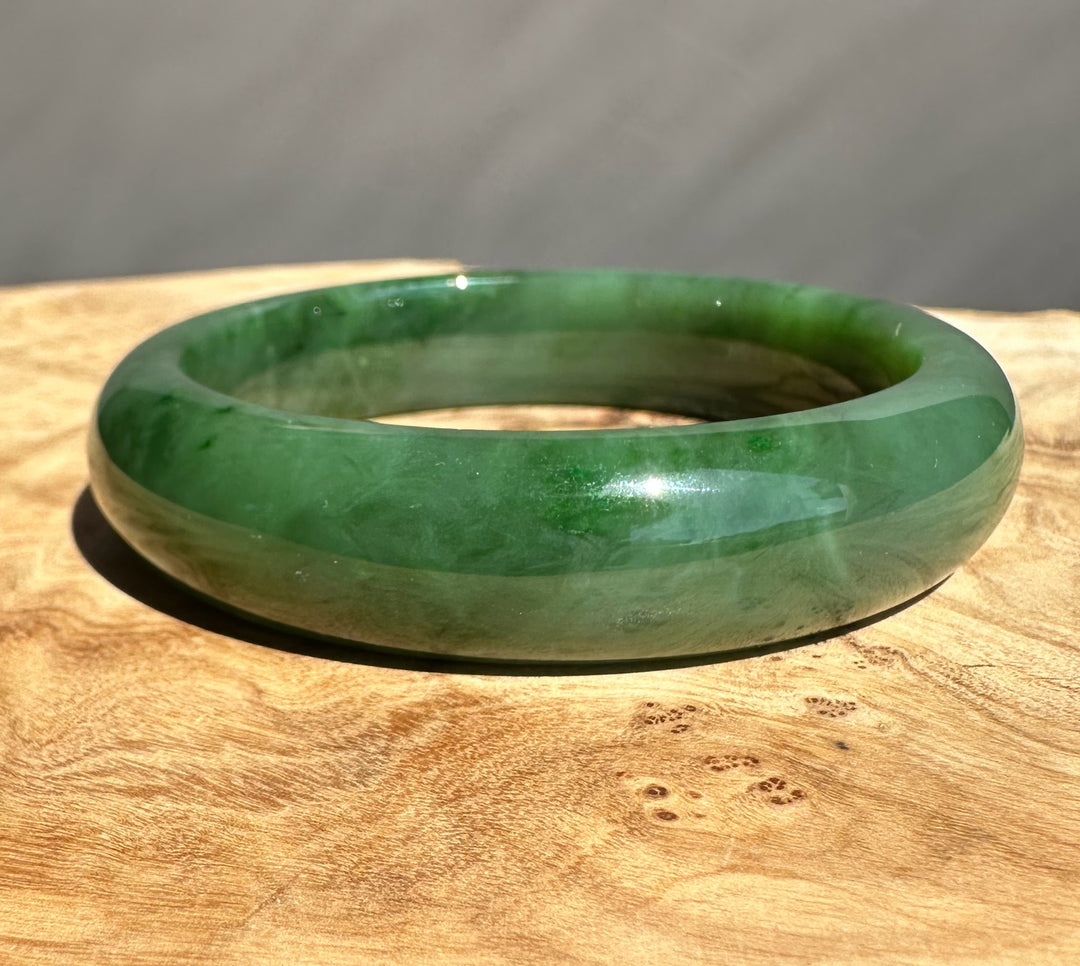 Green jade bangle on a textured wood surface with a gray background, highlighting its rounded silhouette