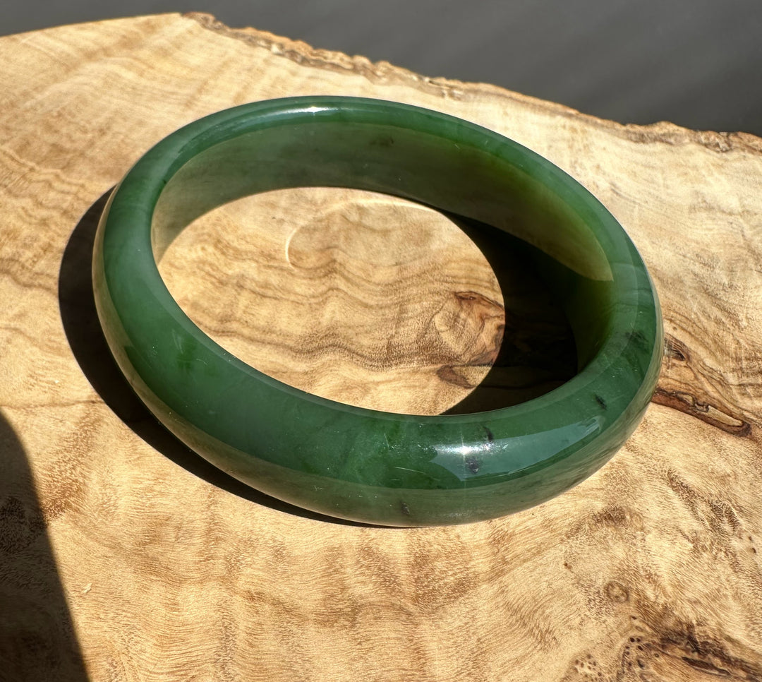 Canadian Jade Bangle in green resting on a warm wood surface, close up on curved edge