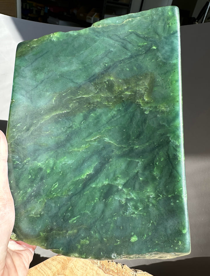 Green jade stone held by a hand against a dark background