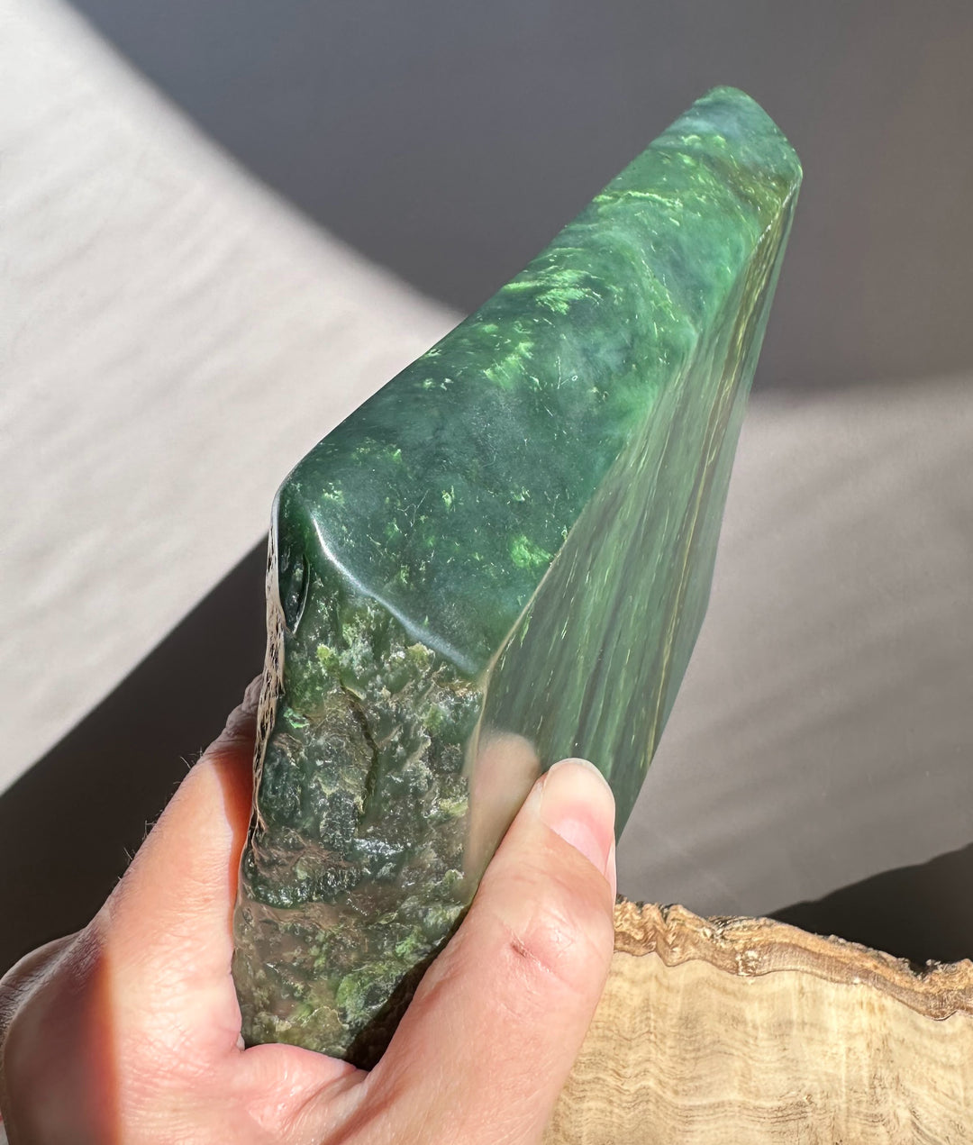 Hand holding a large green stone against a neutral background
