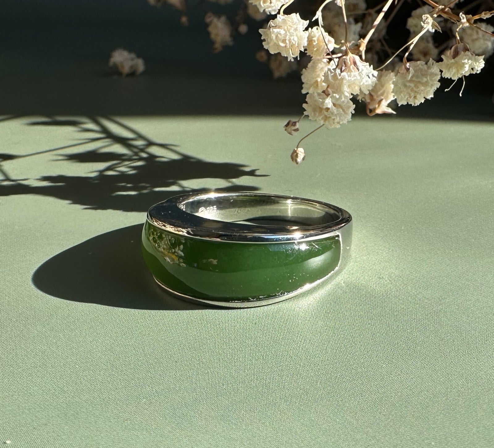 Canadian Jade Ring featuring a thick green jade band in a silver setting on a green surface.
