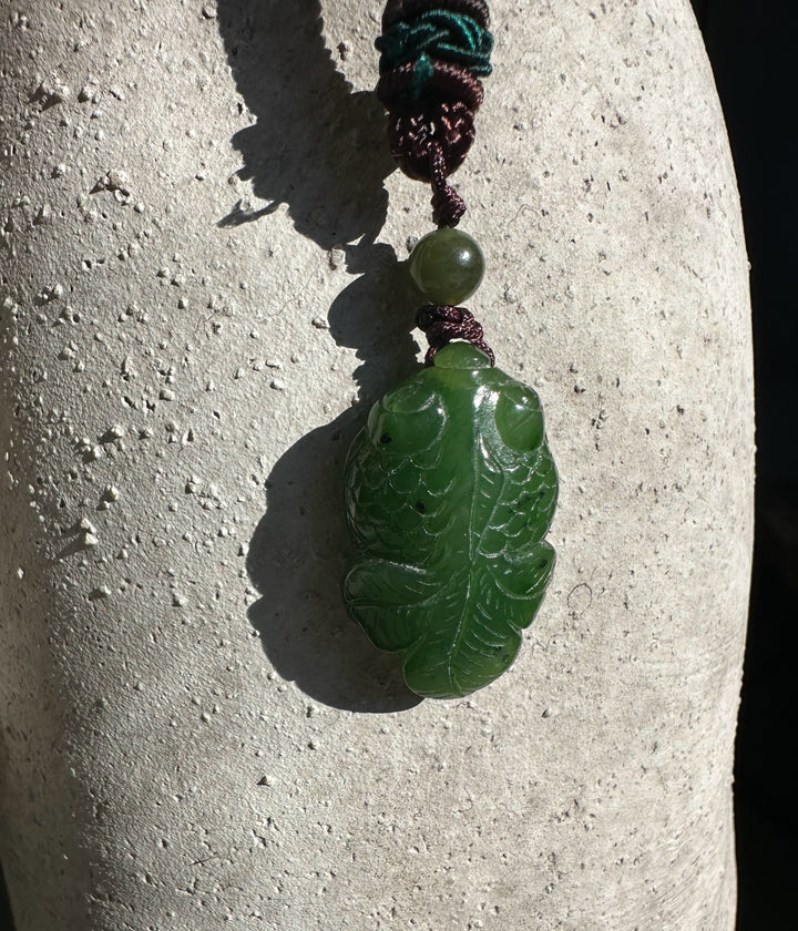 Green jade leaf pendant with carved veins, suspended from a braided cord with a round green bead