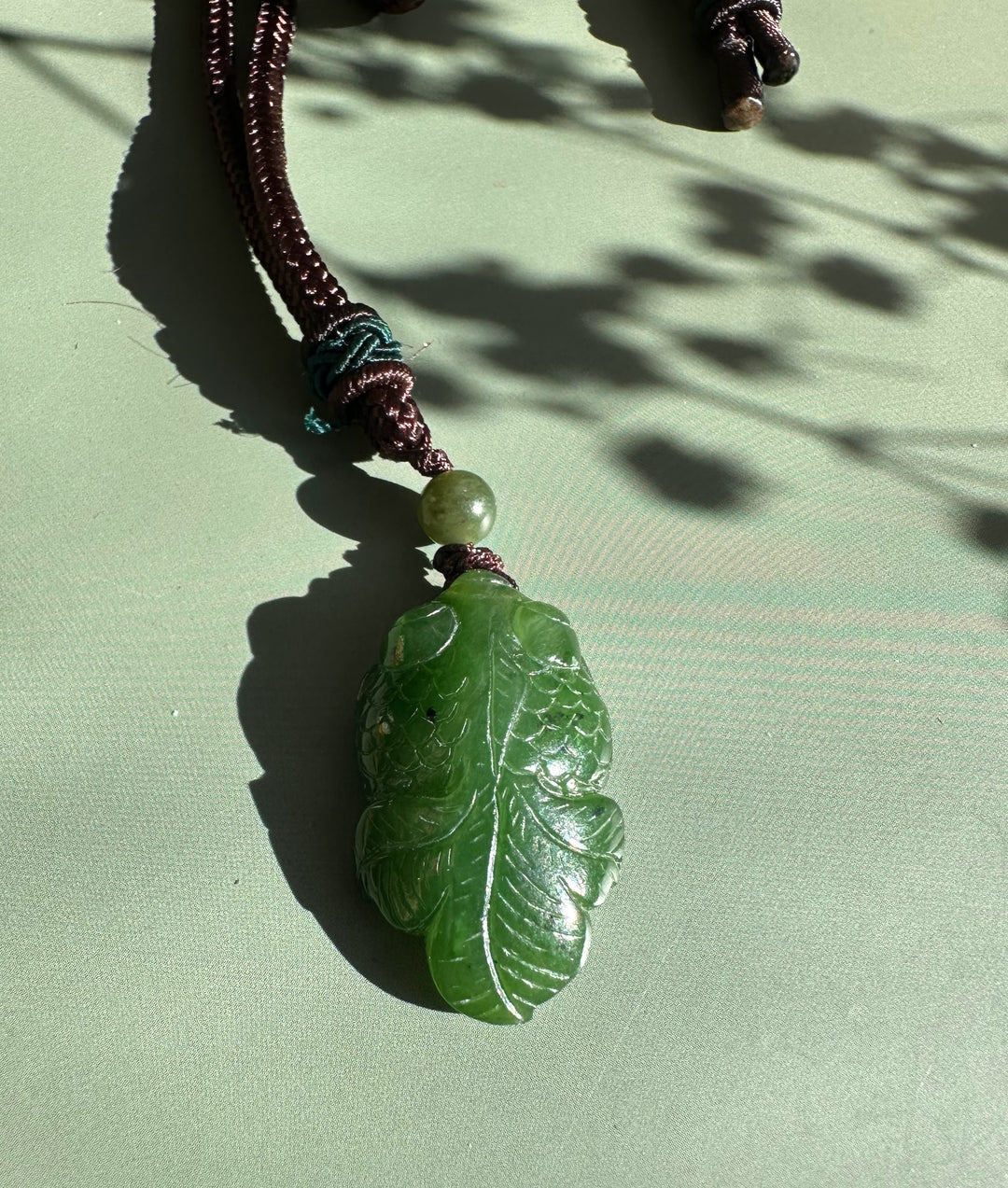Green jade goldfish pendant carved with scales, attached to a brown cord with a pale bead.