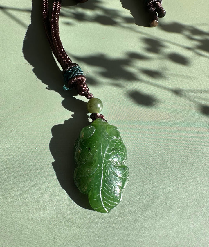 Green jade goldfish pendant carved with scales, attached to a brown cord with a pale bead.