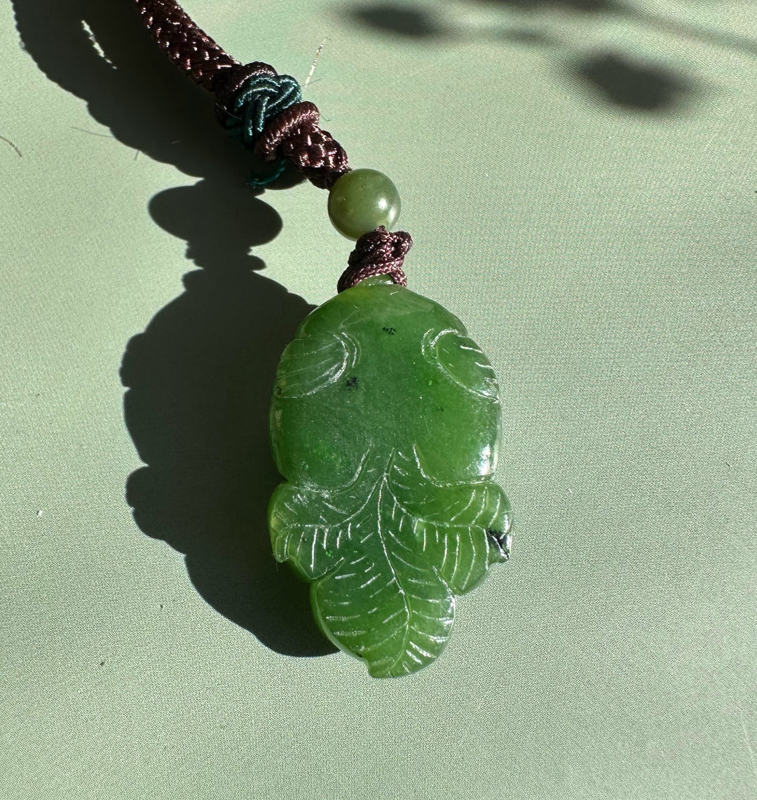 Green jade leaf pendant with vein details on a brown braided cord and a round green bead