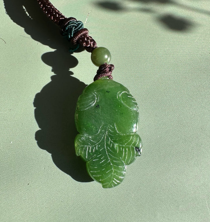 Green jade leaf pendant with vein details on a brown braided cord and a round green bead