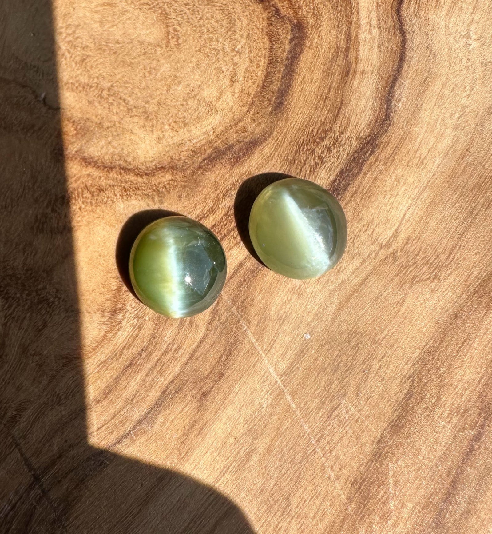 Two green cat's eye gemstones on a wooden surface