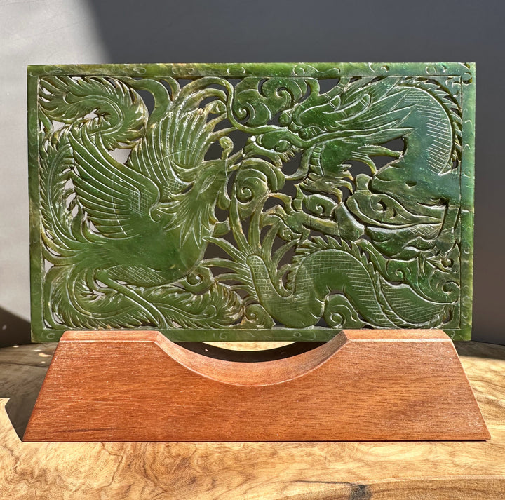 Carved green stone panel with dragon design on a wooden stand against a dark background