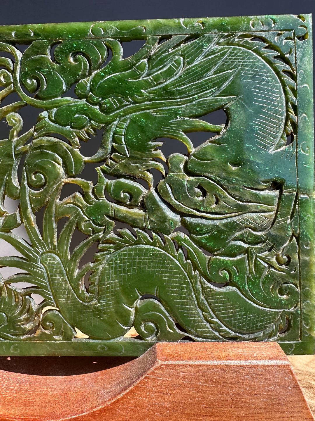 Carved green jade panel with dragon design on a wooden stand