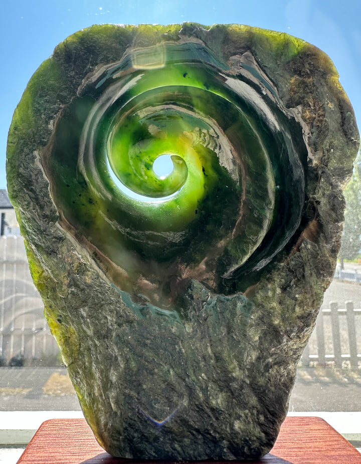 Polar Jade Koru Sculpture 5.8 inches: green spiral carved inside a rugged stone, on a wooden base.