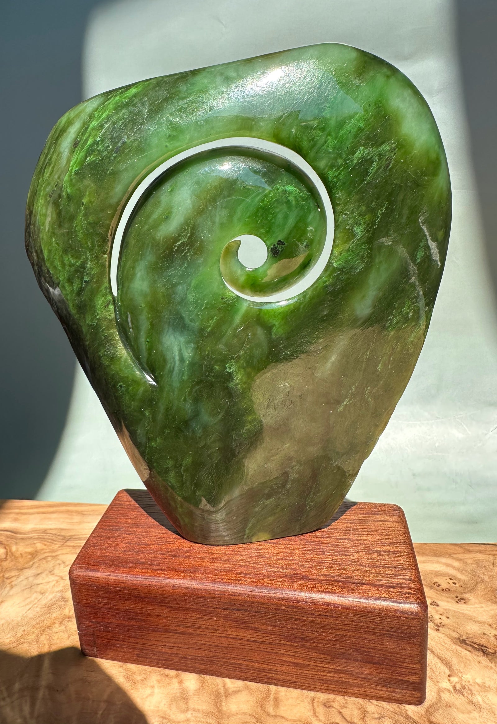 Polished Polar Jade Koru Sculpture in rich green with a white ring accent around the spiral, mounted on a wooden base.