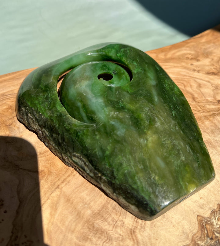 Side view of Polar Jade Koru Sculpture with a rounded green spiral carved into jade, mounted on a wooden base.