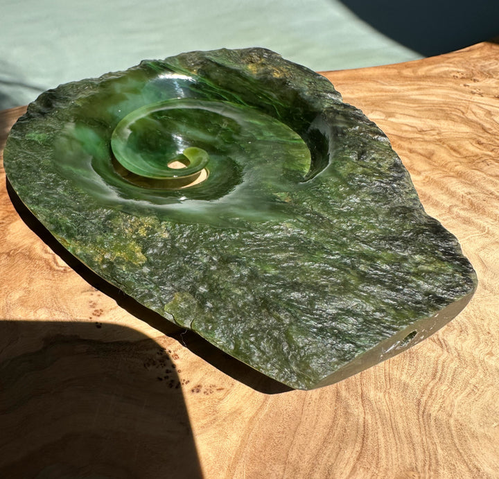Polar Jade Koru Sculpture featuring a smooth green spiral set in a rugged green stone base on a wooden surface.