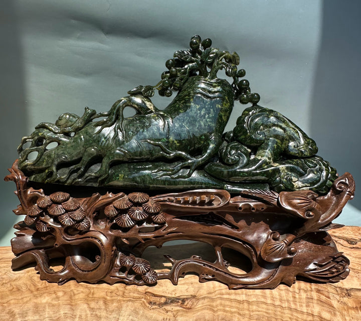Green jade Cassiar sculpture close up shows a tree with round fruit over the reclining beast and a carved wooden base.