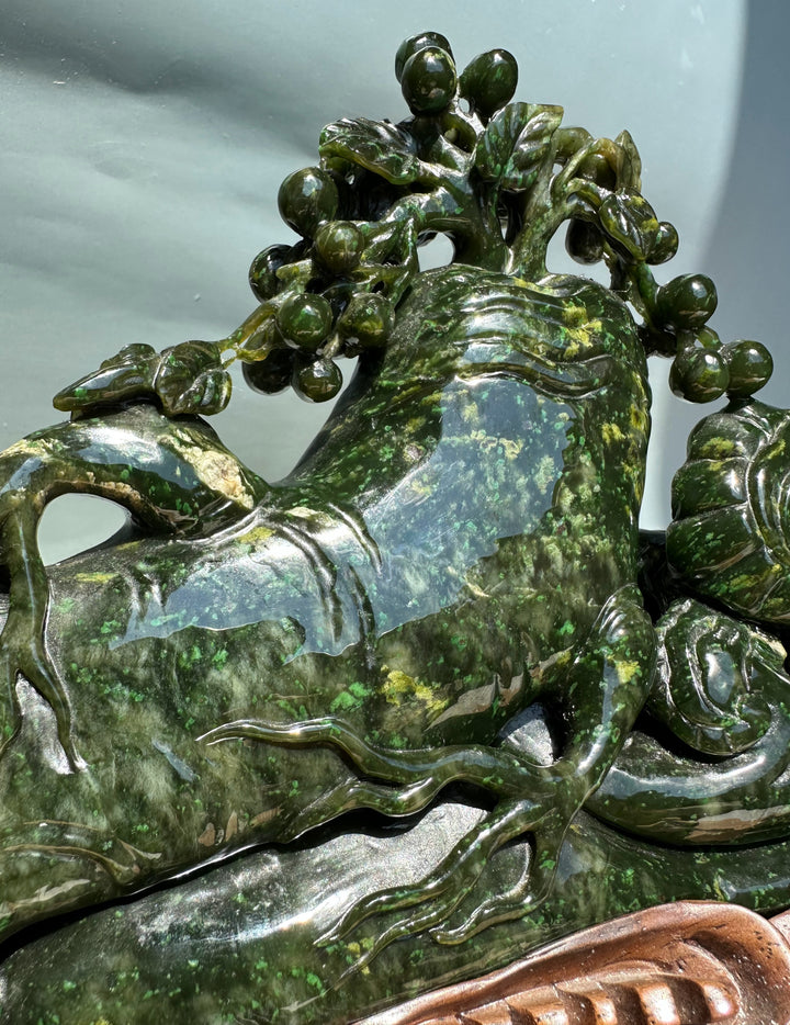 Close-up of the green jade sculpture showing leafy branches and berry clusters on a glossy surface