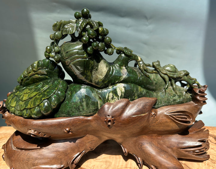 Green jade Cassiar sculpture of a reclining mythical creature with a grapevine crown on a carved wooden base