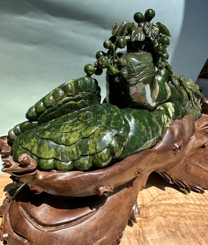 Close up of green jade sculpture showing grape clusters draped over the creature and a carved wooden stand