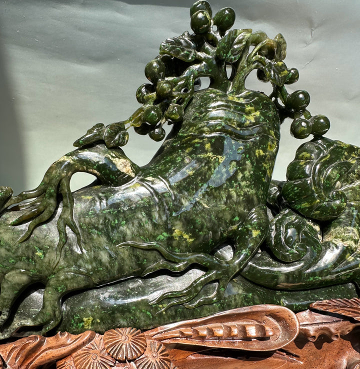 Dark green jade Cassiar sculpture of a gnarled tree with clustered fruit atop a carved wooden base