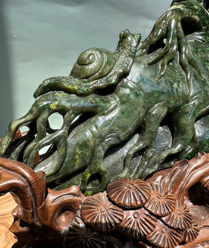 Close-up of dark green jade sculpture showing twisting roots and a decorative motif along the trunk